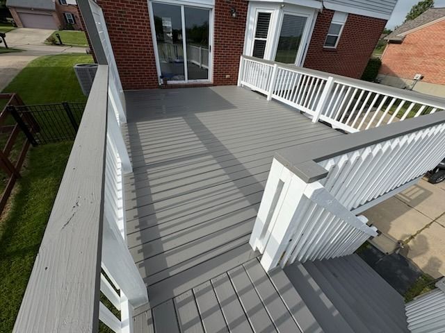 Gray wooden deck with white railing, stairs leading down, and a brick house in the background.