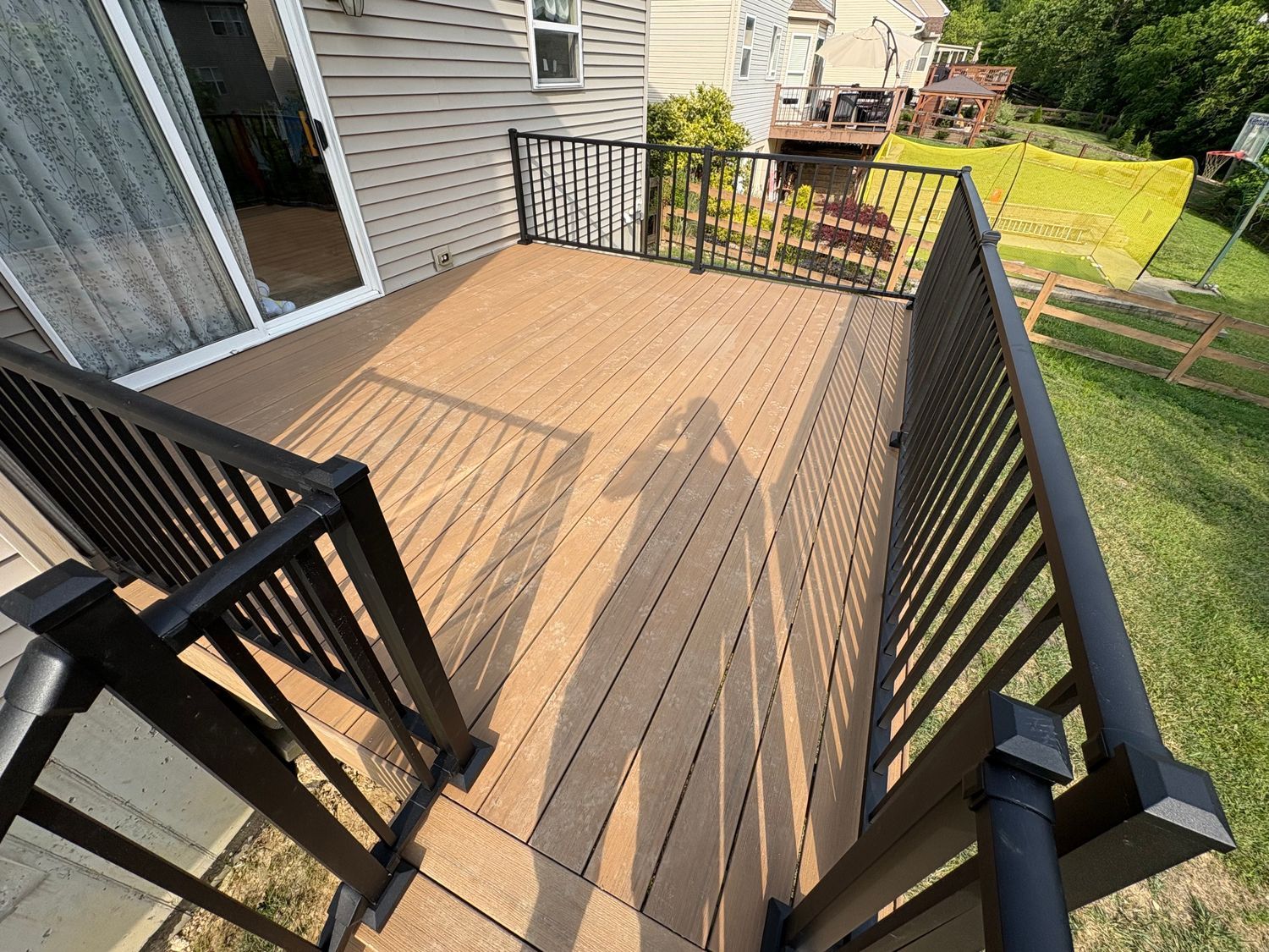 Brown composite deck with black railings in a backyard, sunny day.