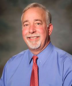 A man in a blue shirt and red tie is smiling for the camera.