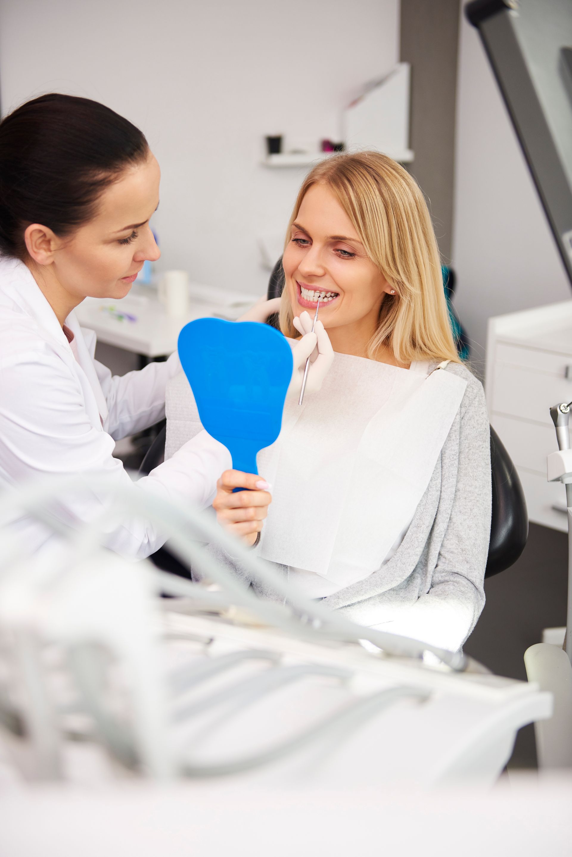 A woman is sitting in a dental chair looking at her teeth in a mirror.