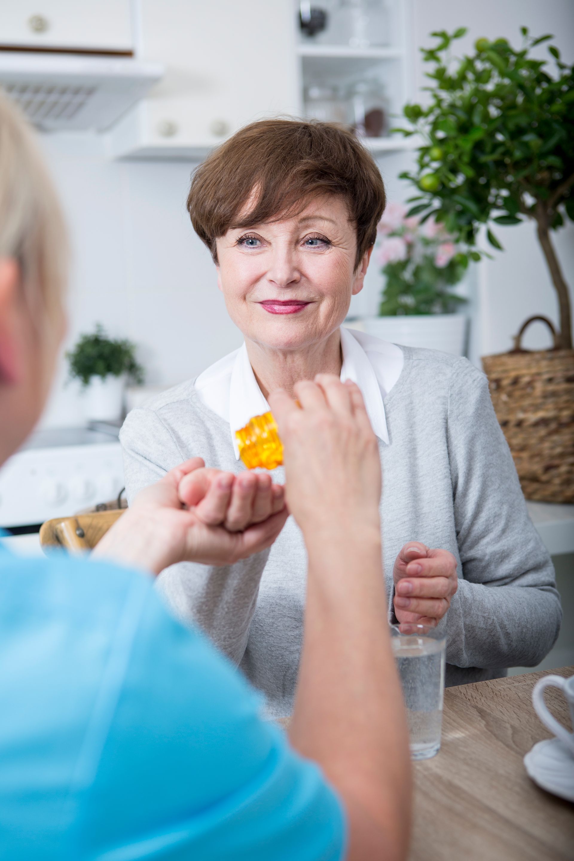 A nurse is giving an elderly woman a pill.