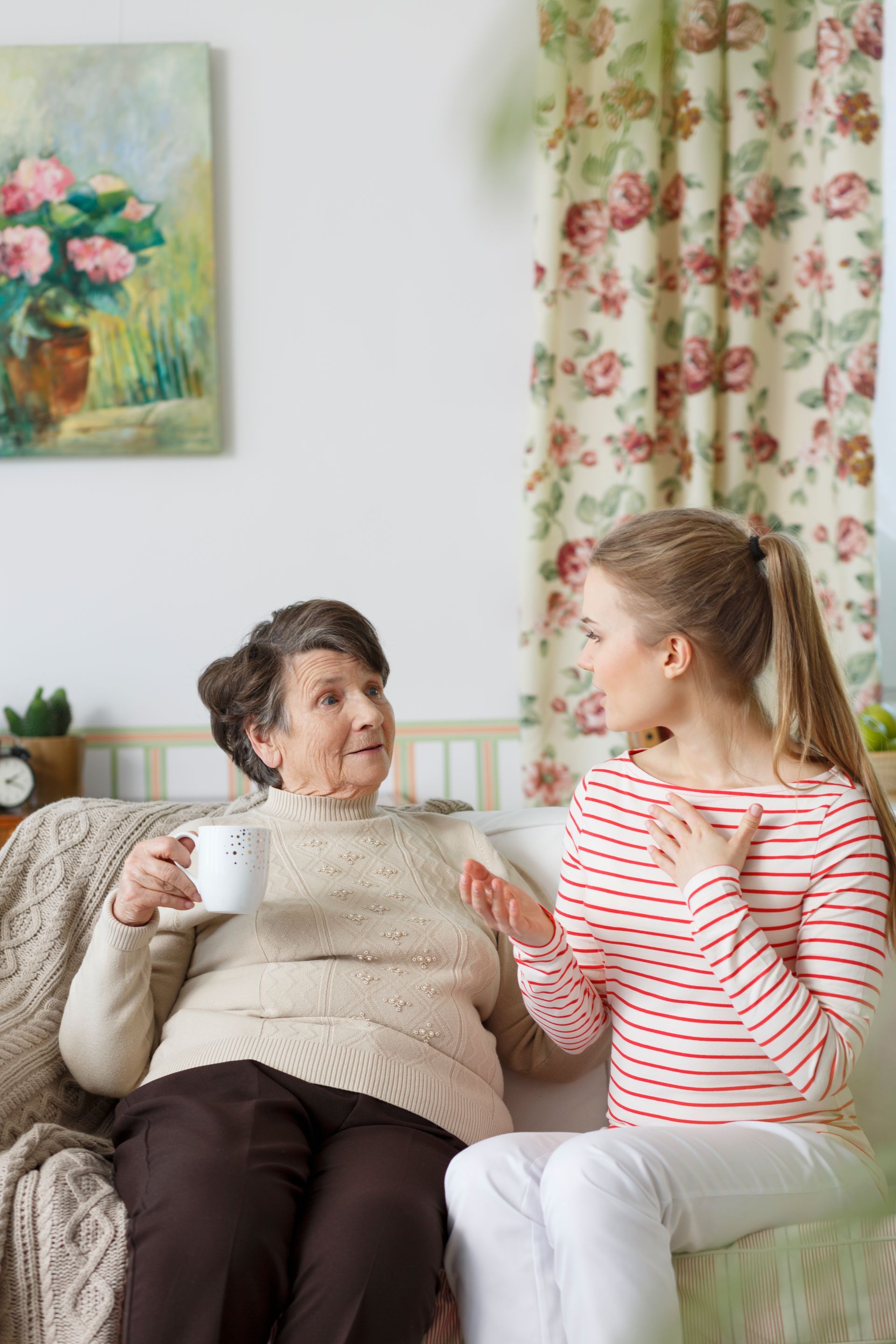 An elderly woman is sitting on a couch talking to a young girl.