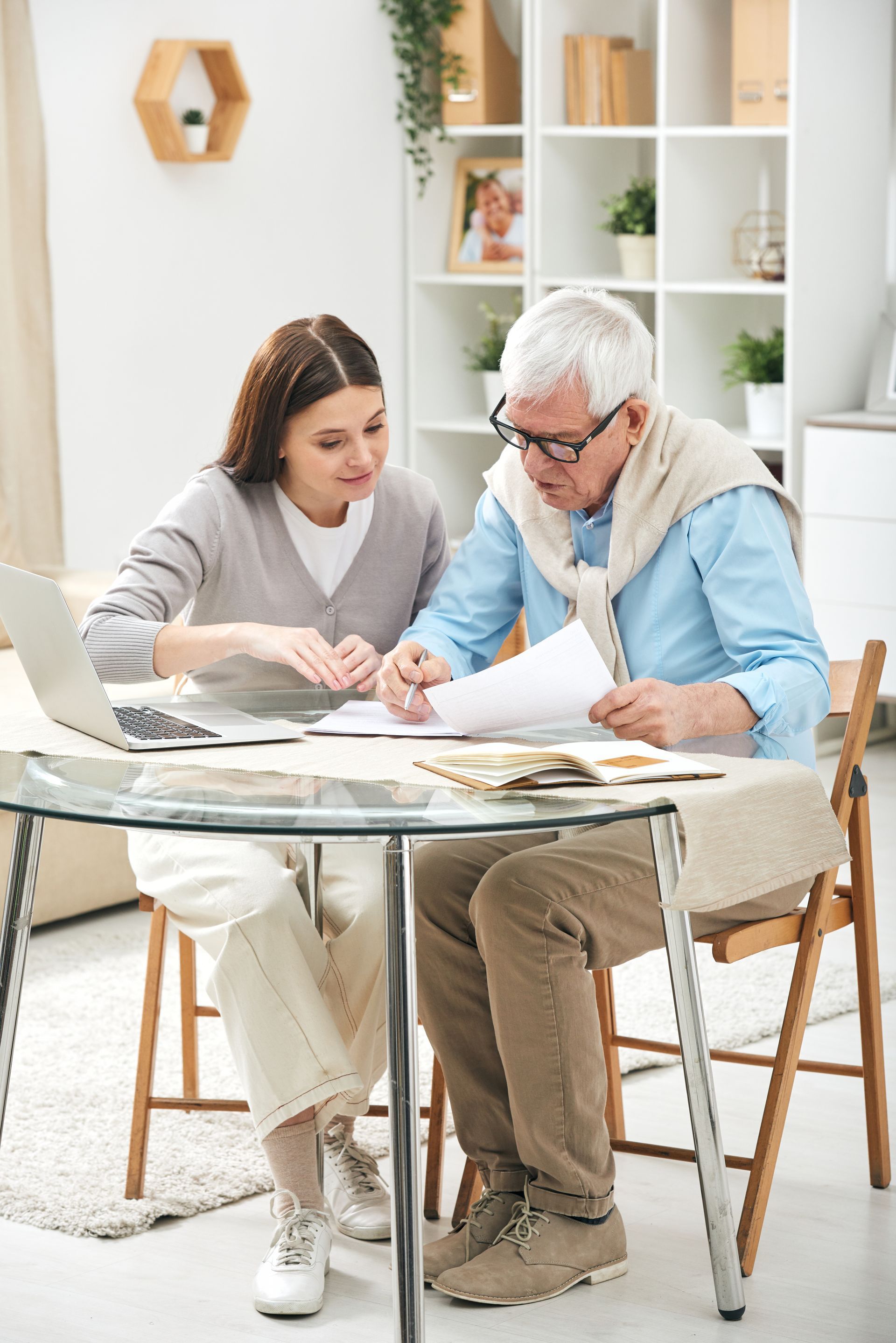 An elderly man and a young woman are sitting at a table looking at papers.