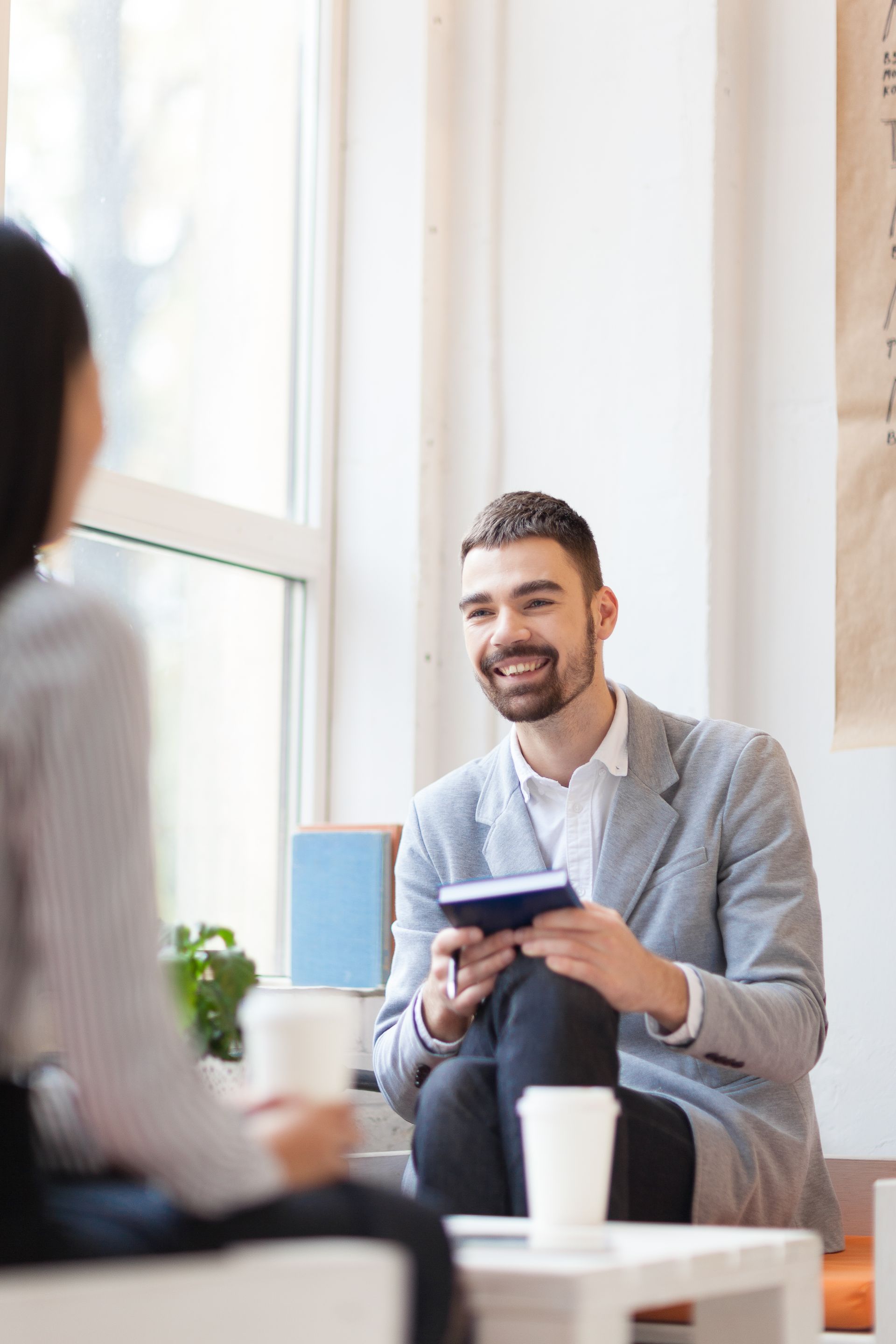 A man is sitting in a chair talking to a woman while holding a book.