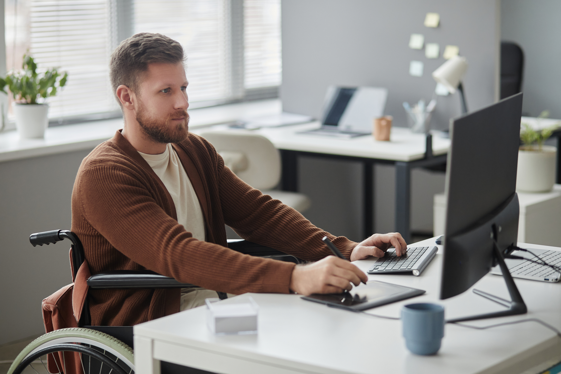 A man in a wheelchair is sitting at a desk using a computer.