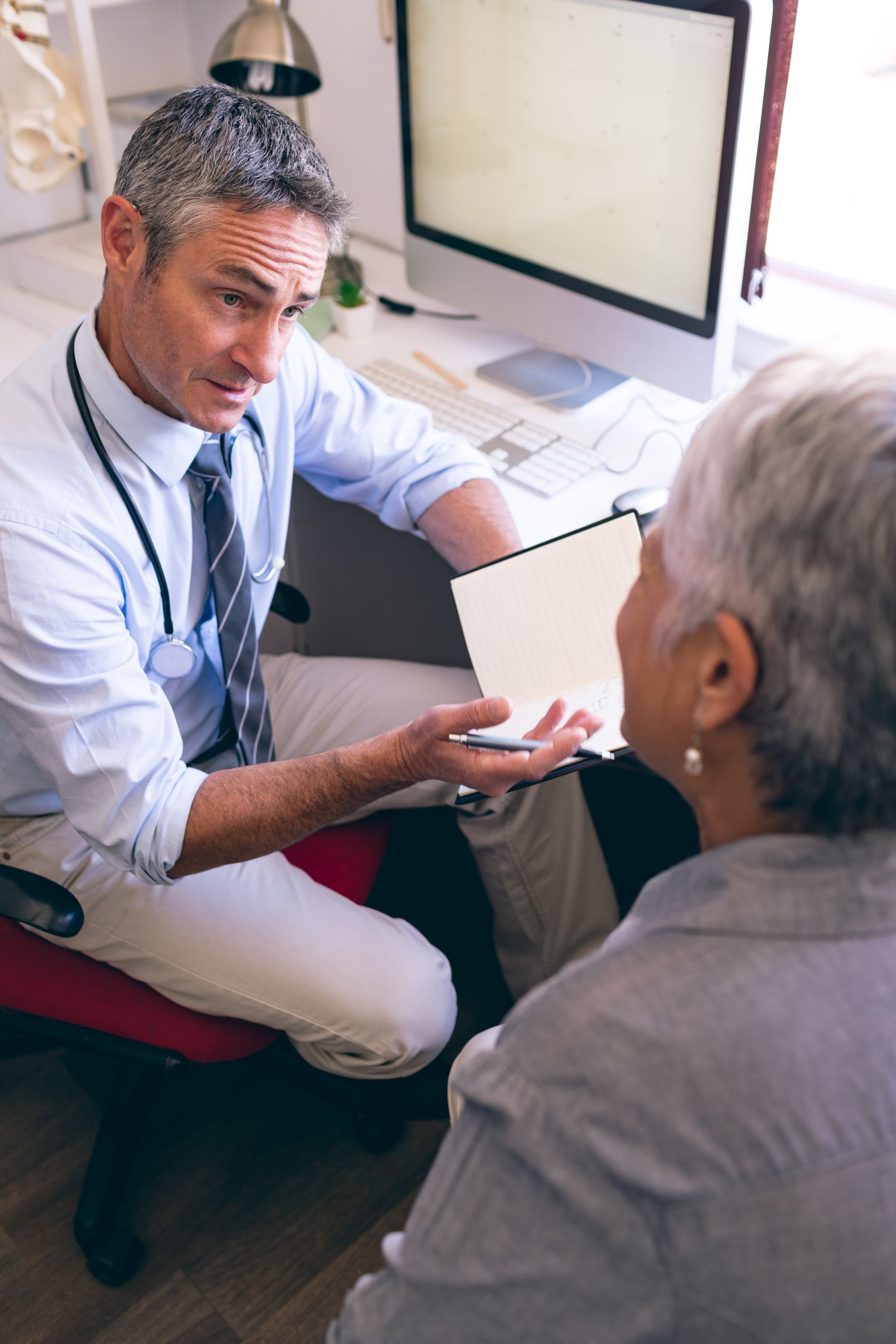 A doctor is talking to an elderly woman in front of a computer.