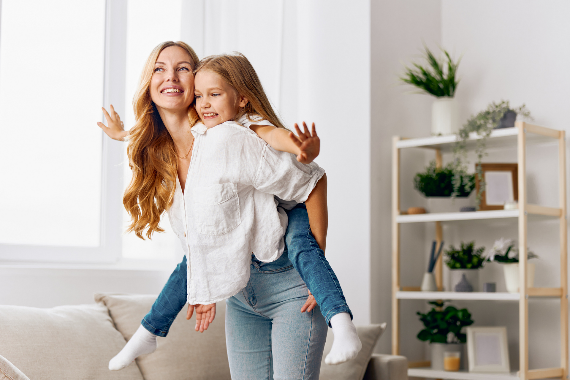 A woman is carrying a little girl on her back in a living room.