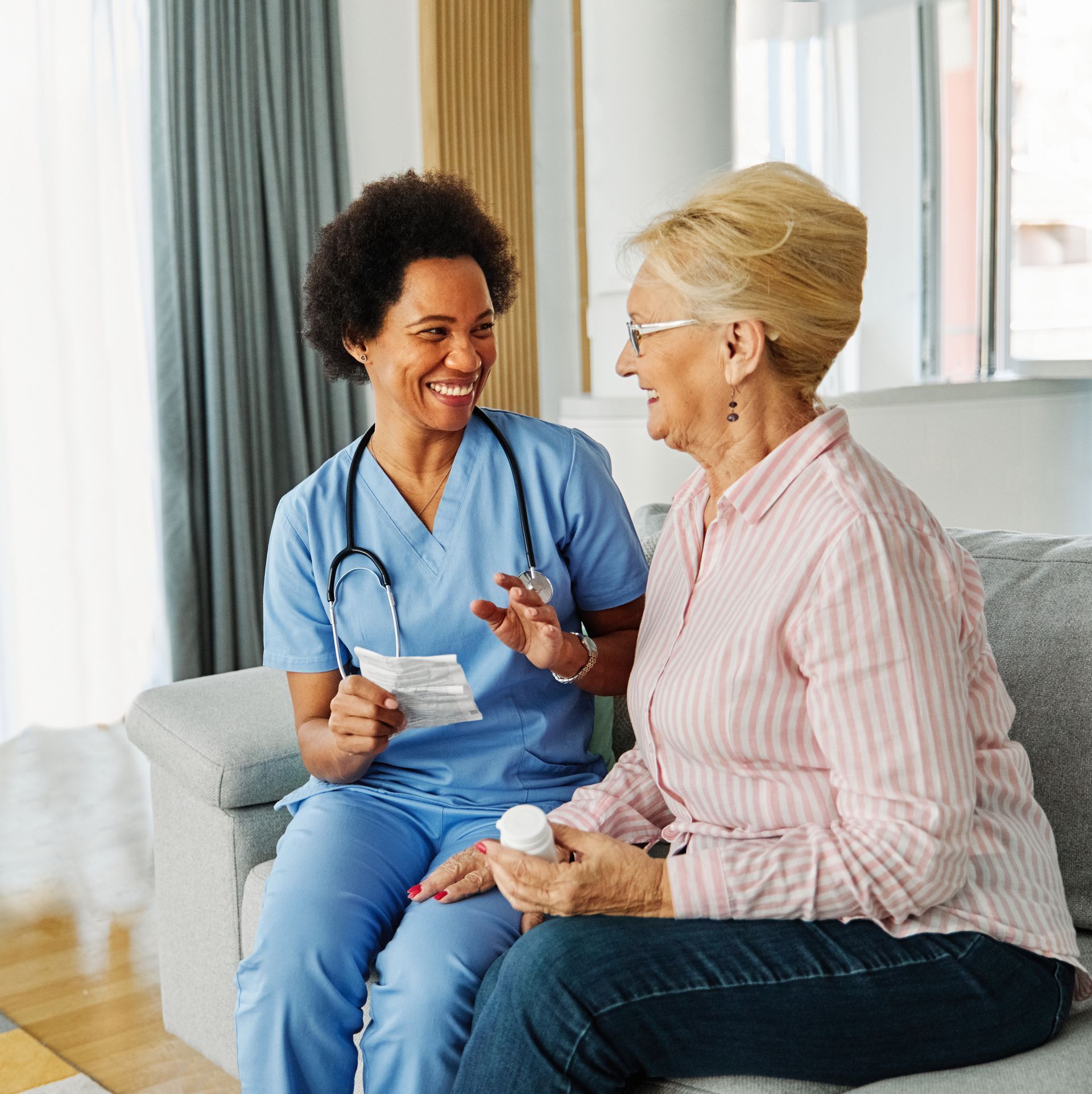 A nurse is sitting on a couch talking to an older woman.