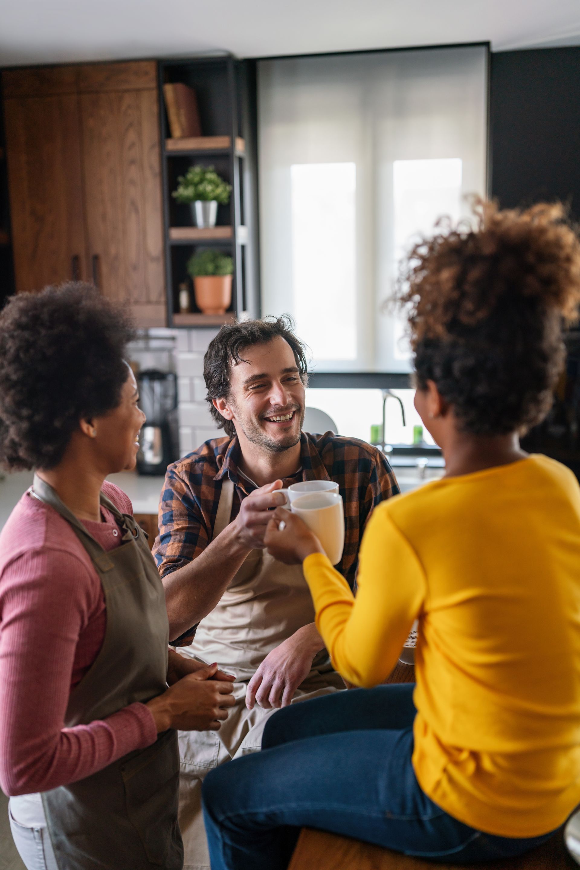 A group of people are sitting at a table in a kitchen talking to each other.