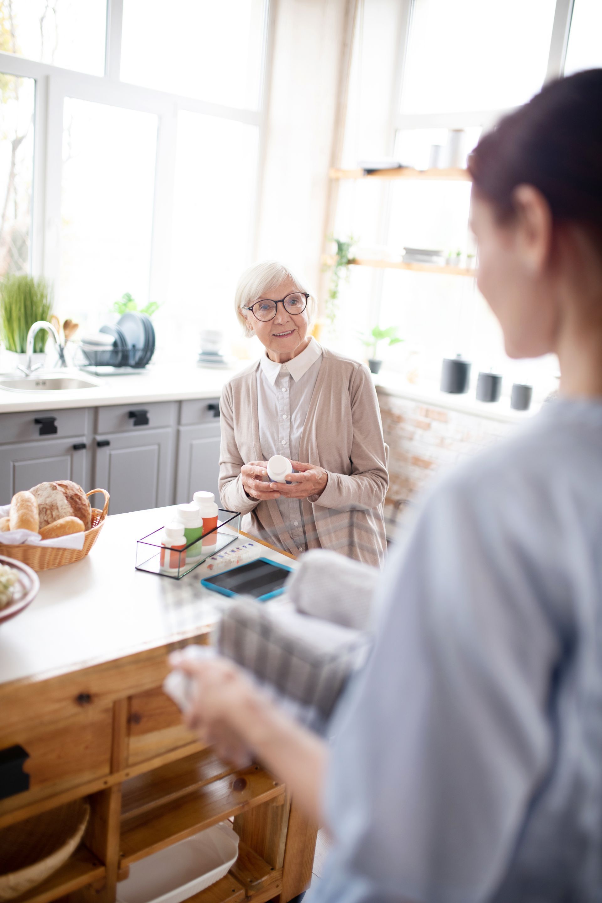 An elderly woman is sitting at a table in a kitchen talking to a nurse.