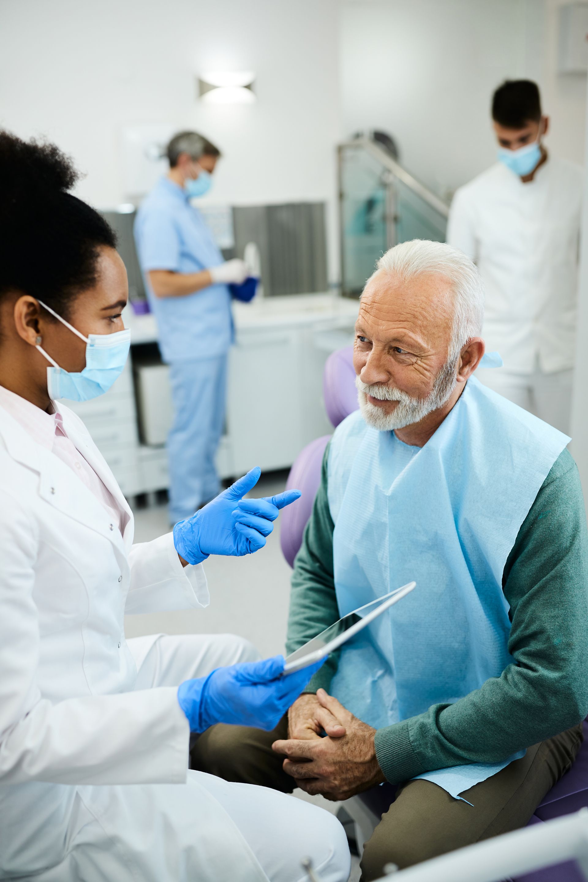 An elderly man is sitting in a dental chair talking to a female dentist.