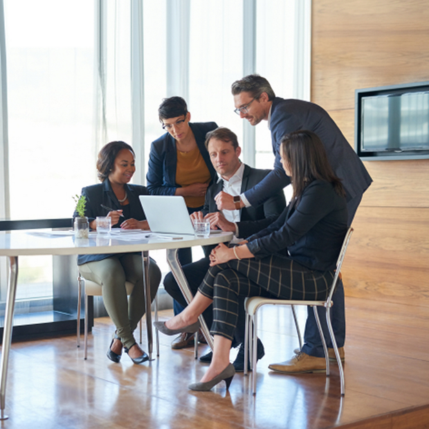 A group of people are sitting around a wooden table having a meeting.