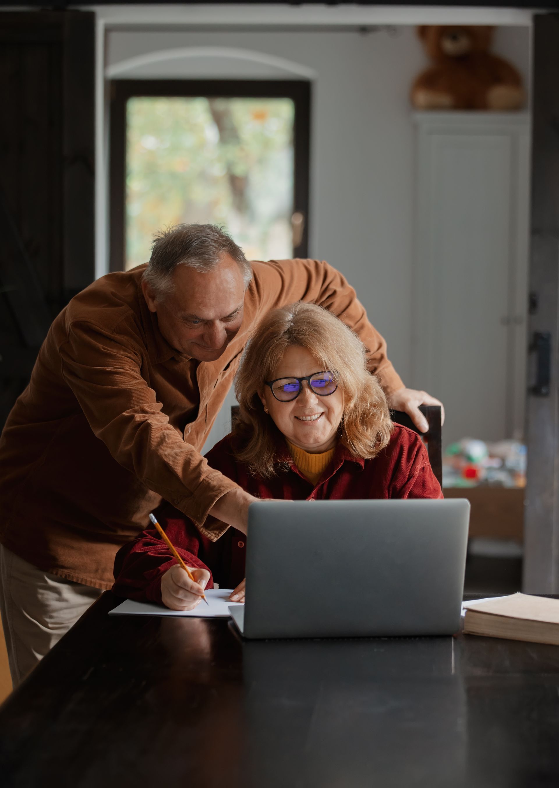 An elderly couple is sitting at a table looking at a laptop computer.