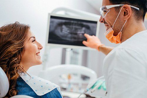 Male dentist pointing at X-rays to female patient
