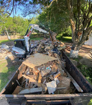 Yellow excavator demolishing a wooden structure under a blue sky.