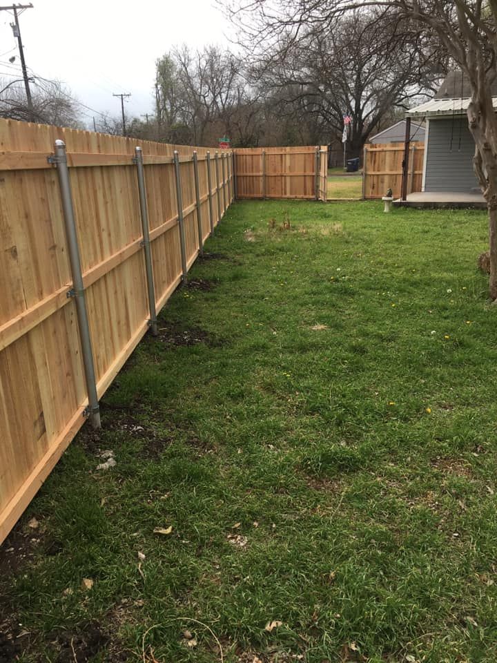 Wooden fence bordering a green grassy yard on a cloudy day.