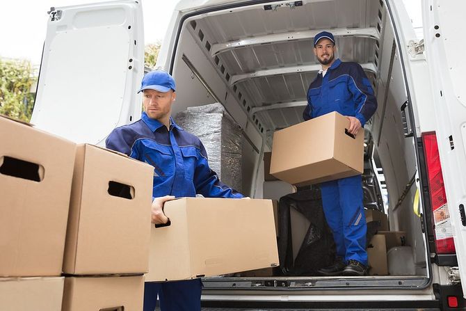 Two professional movers in blue uniforms loading cardboard boxes into a white delivery van.