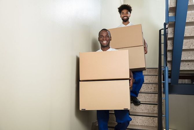 Two smiling movers carrying cardboard boxes down stairs.