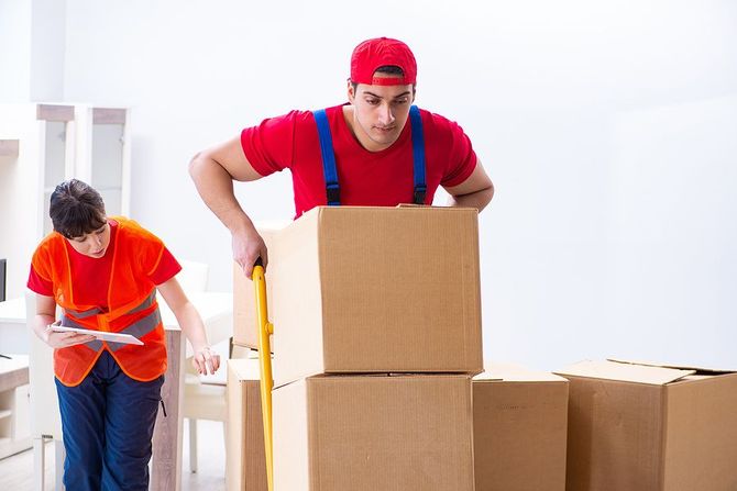 Professional movers loading cardboard boxes onto a yellow hand truck.