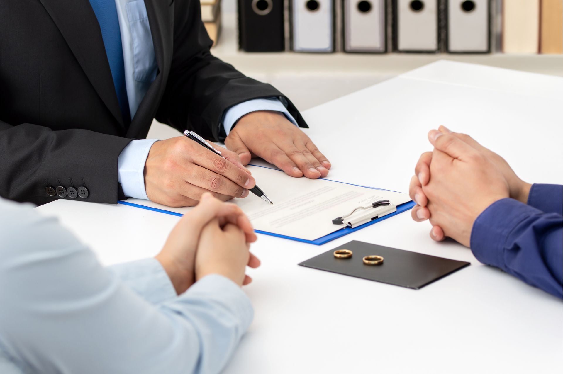 Divorce attorney mediating tense couple with wedding ring on table, reviewing divorce documents.