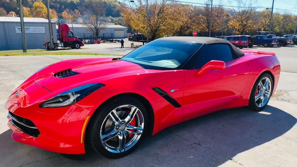 Red Chevrolet Corvette convertible parked, sunny outdoor setting.