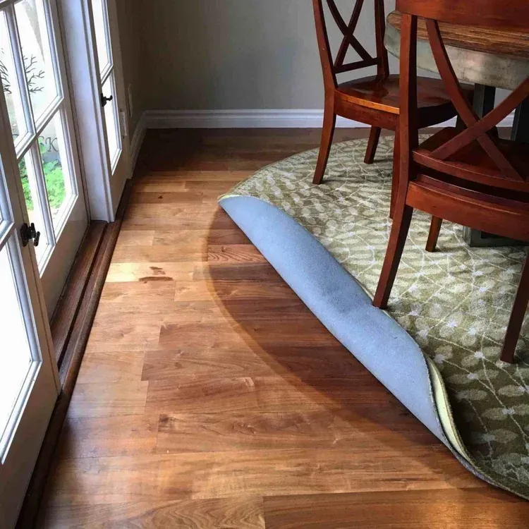 Wooden floor with rolled-up area rug; chairs and table in dining room near a door.