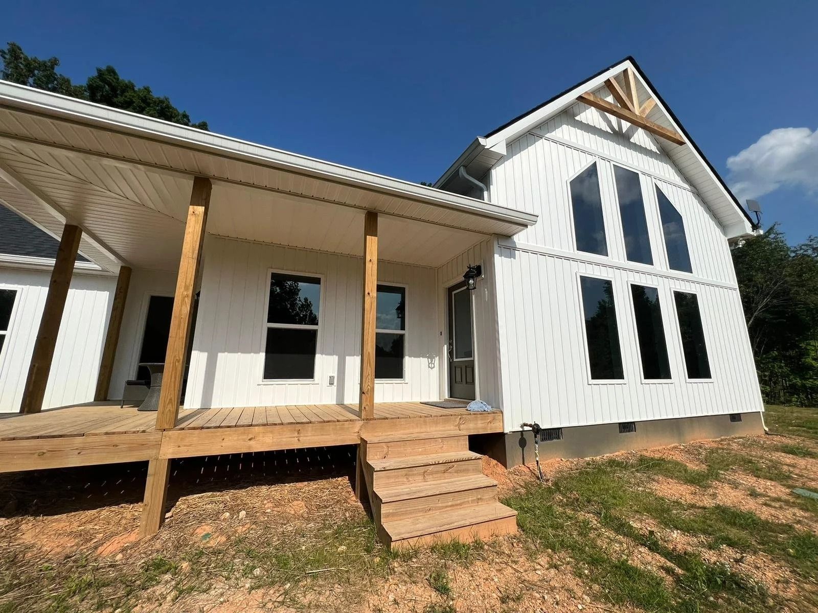 White house with porch, steps, and large black windows under a blue sky.