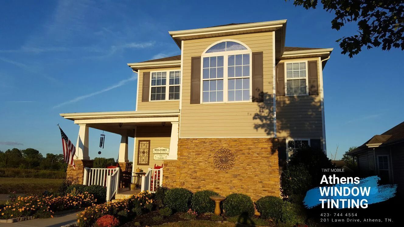 Beige two-story house with window tinting, brown shutters, and American flag on the porch.