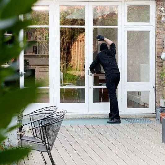 Person in black attempting to open a glass door with white frame from outside on a wooden deck.