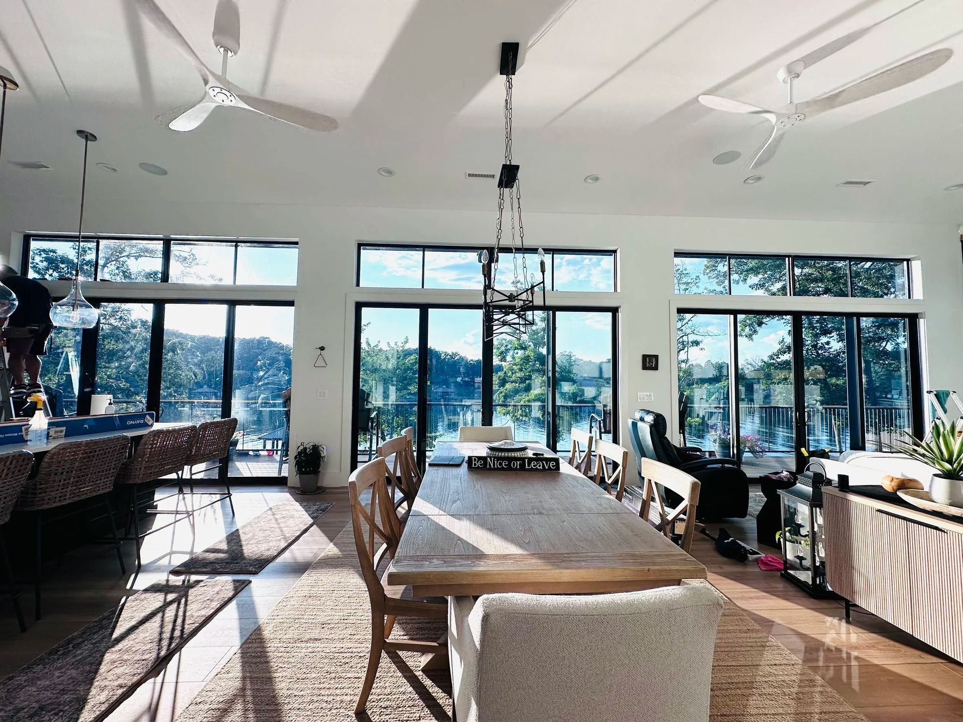 Dining room with long wooden table and chairs, large windows overlooking water, ceiling fans.