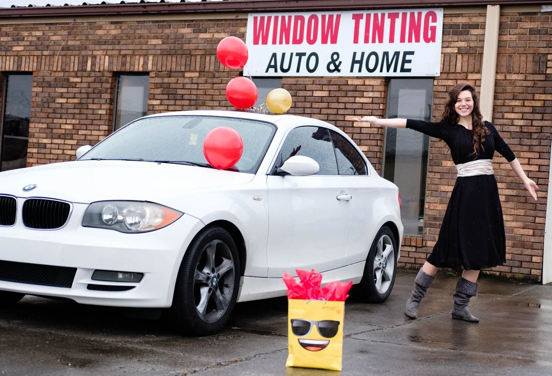 Woman celebrating beside a white car with balloons, in front of a window tinting shop.