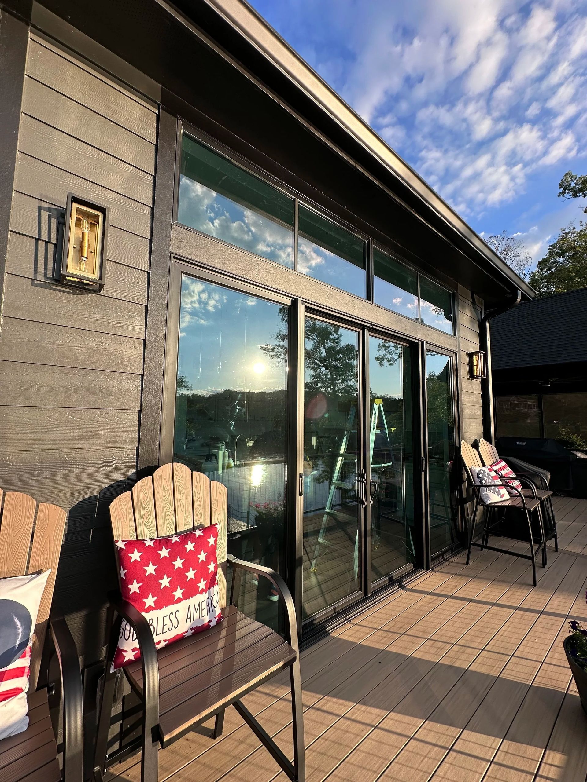 Patio with glass doors, chairs with patriotic pillows, and a view of a lake with a sunny sky.