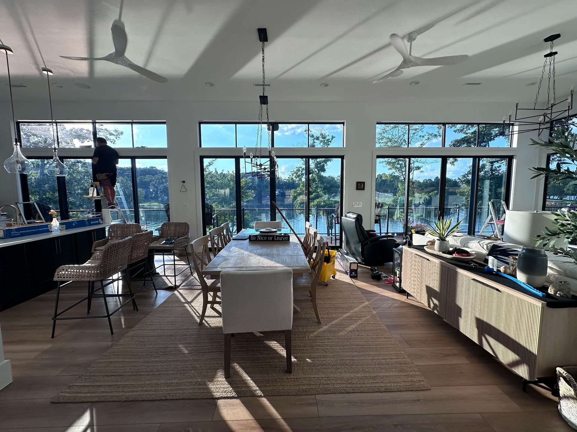 Bright interior with large windows overlooking a lake. A person on a ladder is working on the ceiling.
