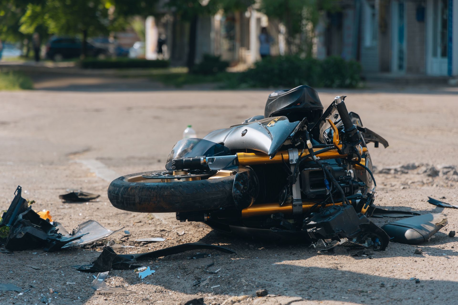 A severely damaged motorcycle lies on its side on a paved street, surrounded by debris from a crash.