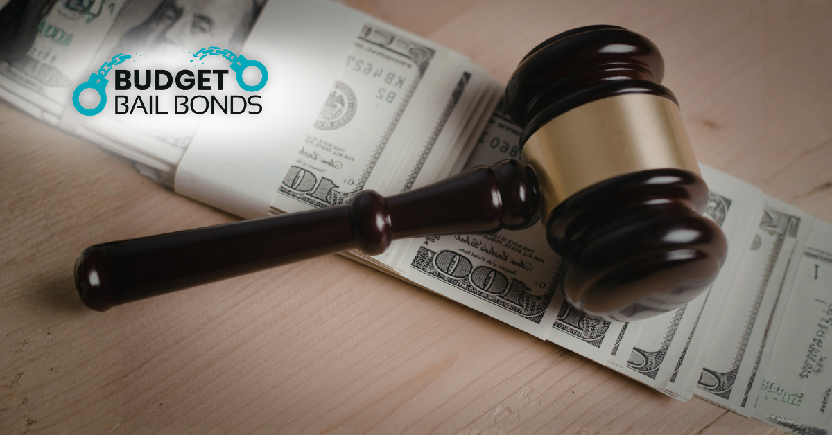 A wooden judge's gavel rests on a stack of US hundred-dollar bills, with the Budget Bail Bonds logo in the corner.