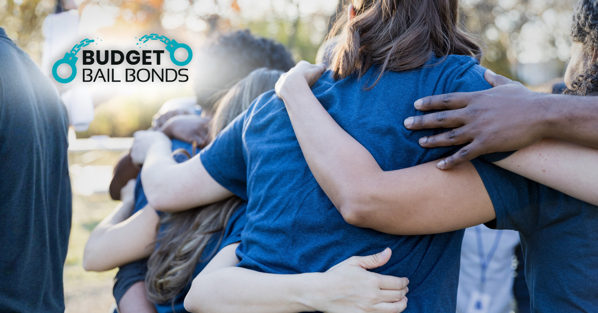 A group of people in blue shirts stand in a circle with their arms around each other. The Budget Bail Bonds logo.