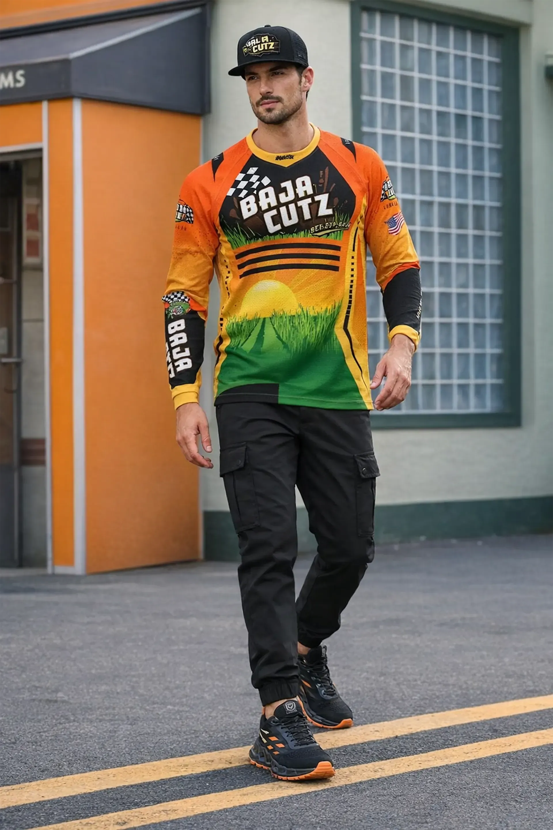 A person wearing a "Baja Cutz" graphic long-sleeve shirt, black cargo joggers, and a baseball cap walking outdoors.