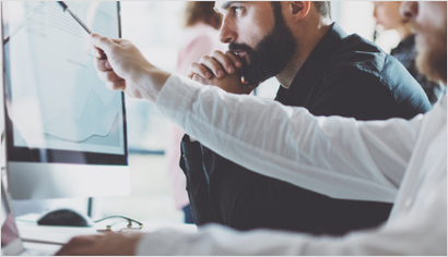 A man with a beard is pointing at a computer screen.