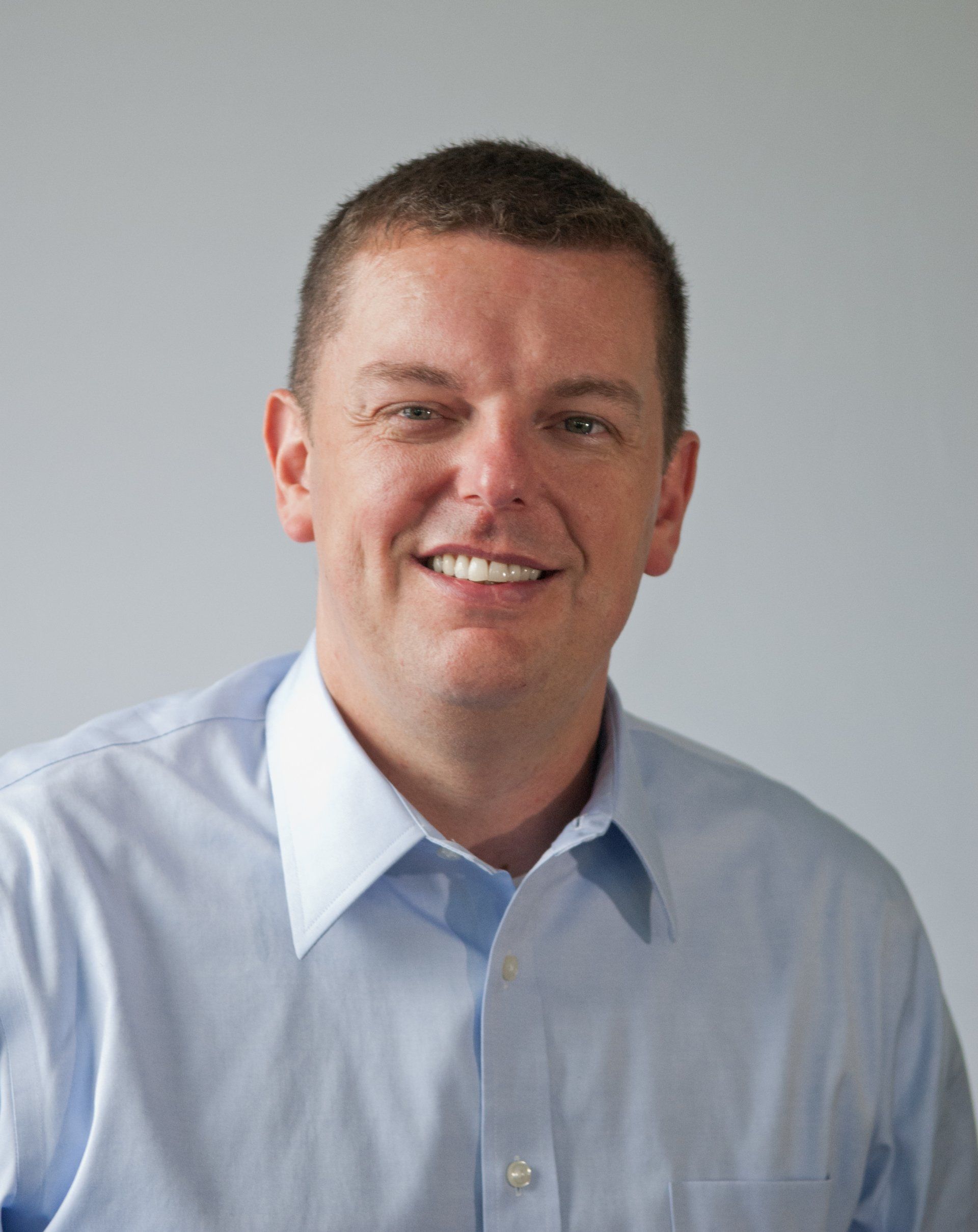 Man with short brown hair and blue shirt smiling at the camera.