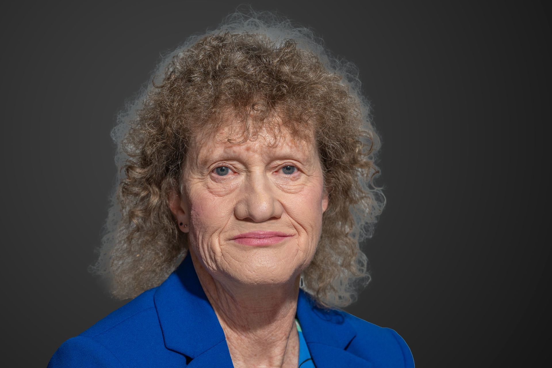 Woman with curly blonde hair in a blue blazer, neutral background.
