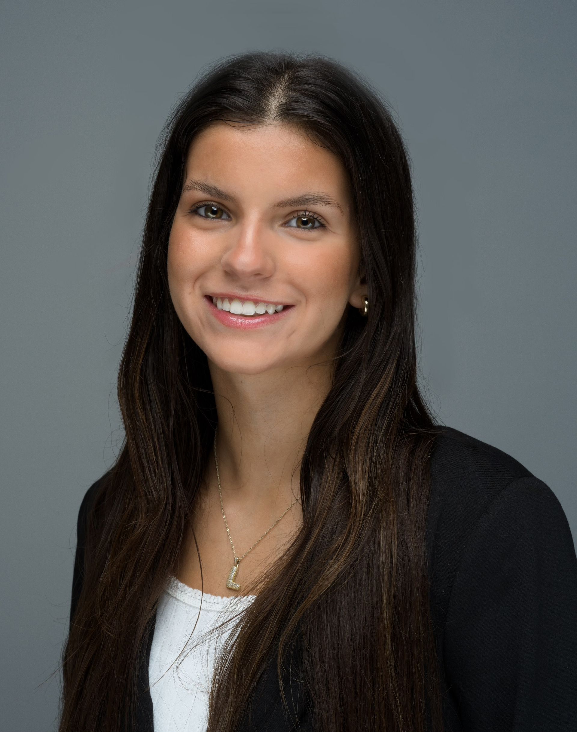 Woman with long brown hair smiling, wearing a black blazer and white top.