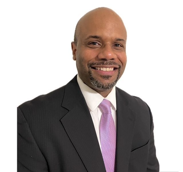 Bald Black man in a suit and tie smiling at the camera.