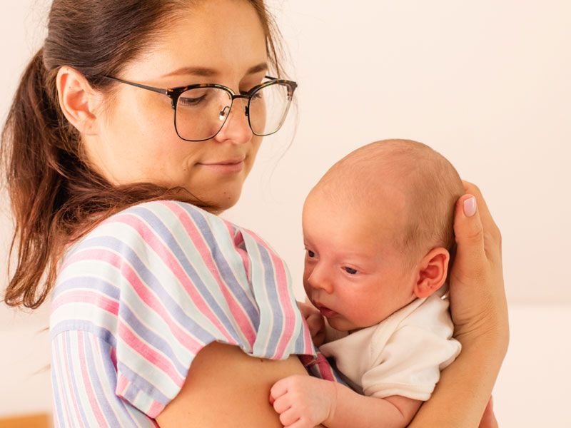 Mother with shoulder pain struggling to hold infant.