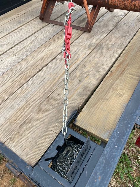 Chain hanging into a storage box on a trailer deck with wooden planks. Red hooks and chain visible.