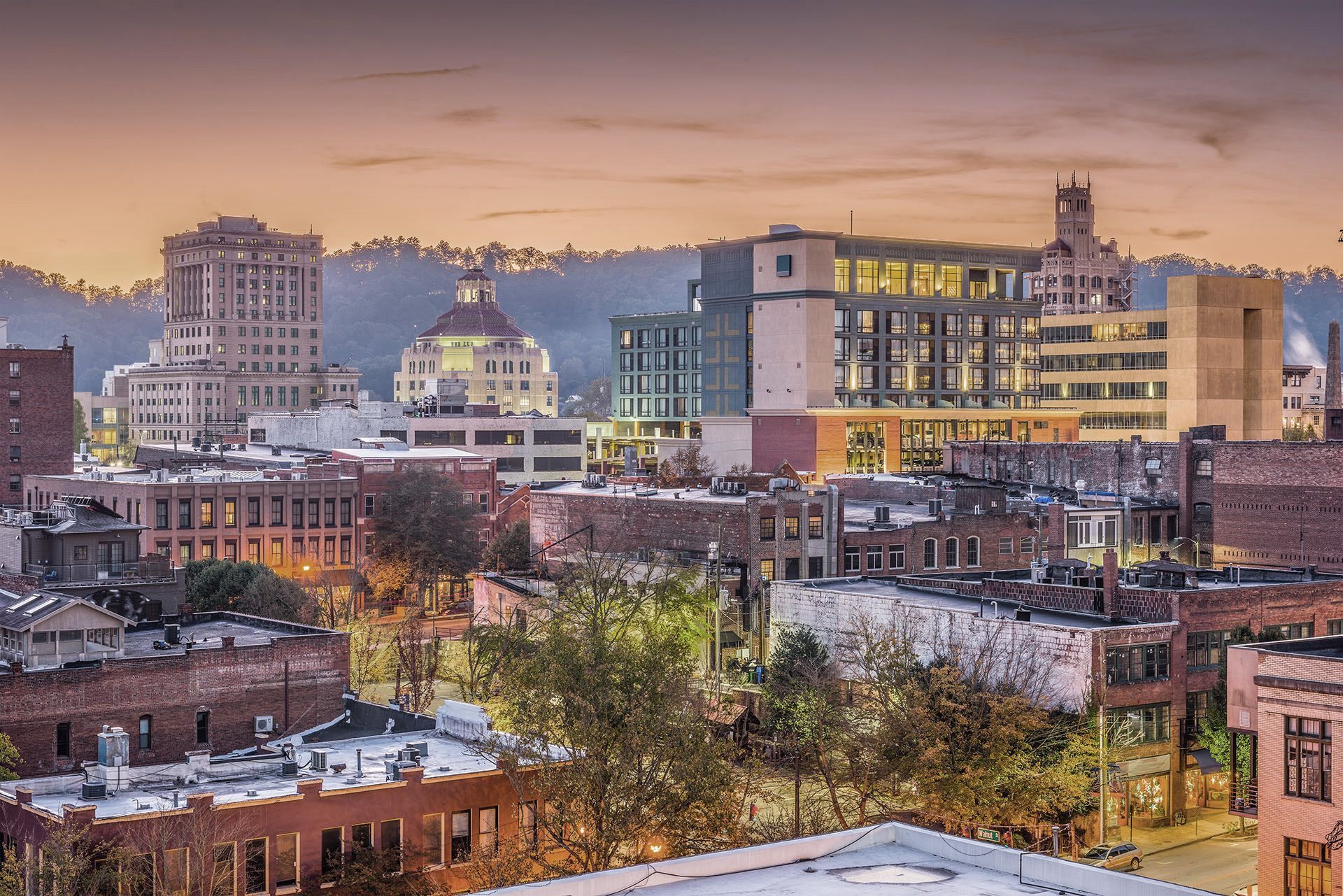 Group of people standing on a grassy hilltop overlooking mountain range at sunrise.