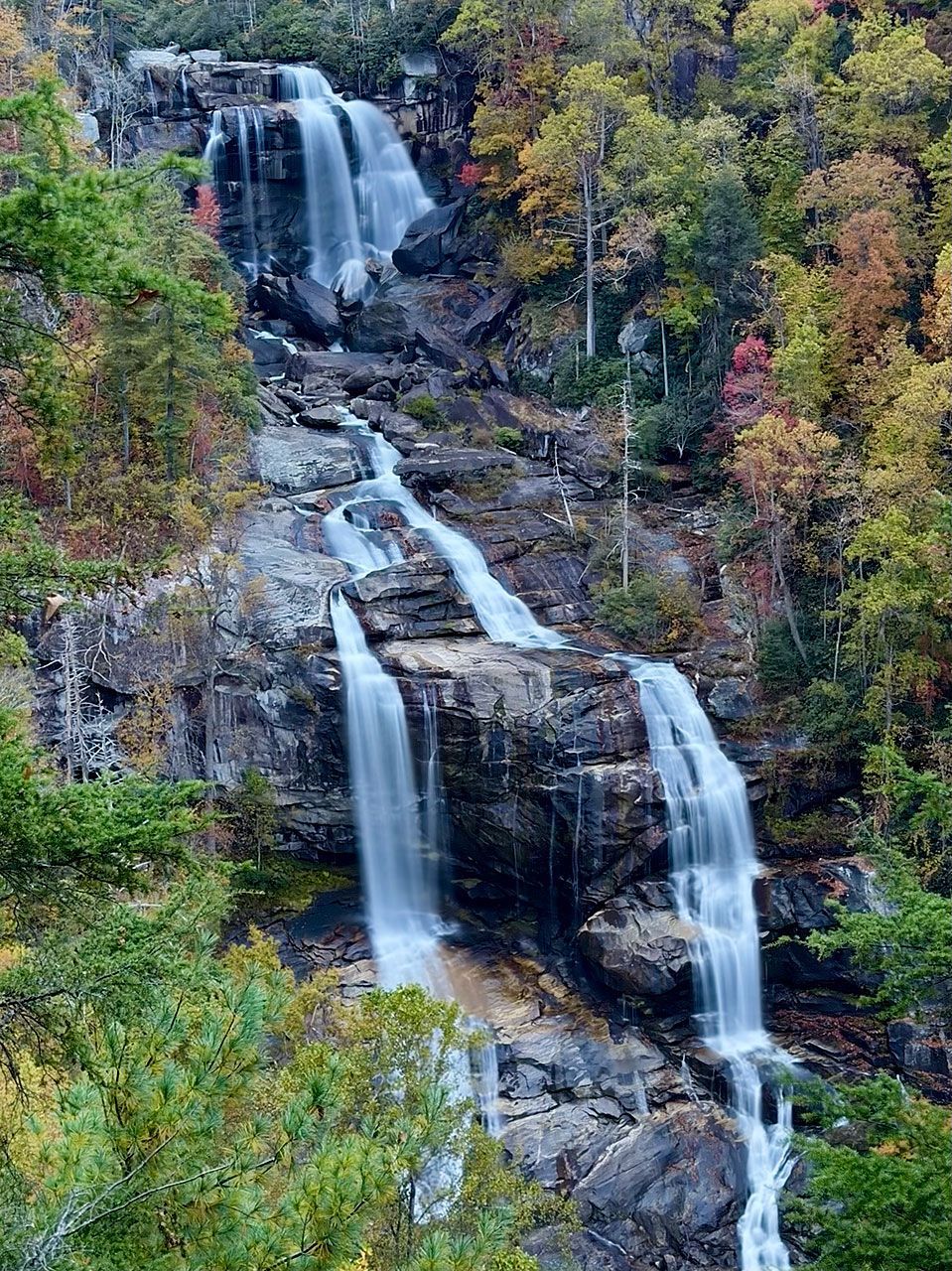Monochrome mountain range with hazy valleys under a pale sky, silhouetted trees in foreground.