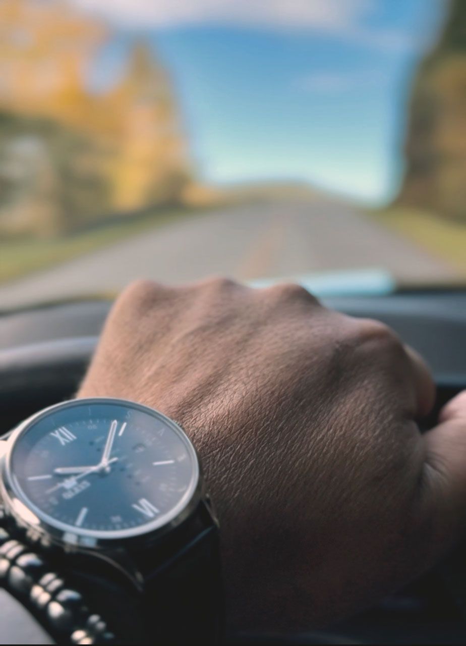 Man in suit, with luggage and bag, looking at phone in hotel lobby; receptionist in background.