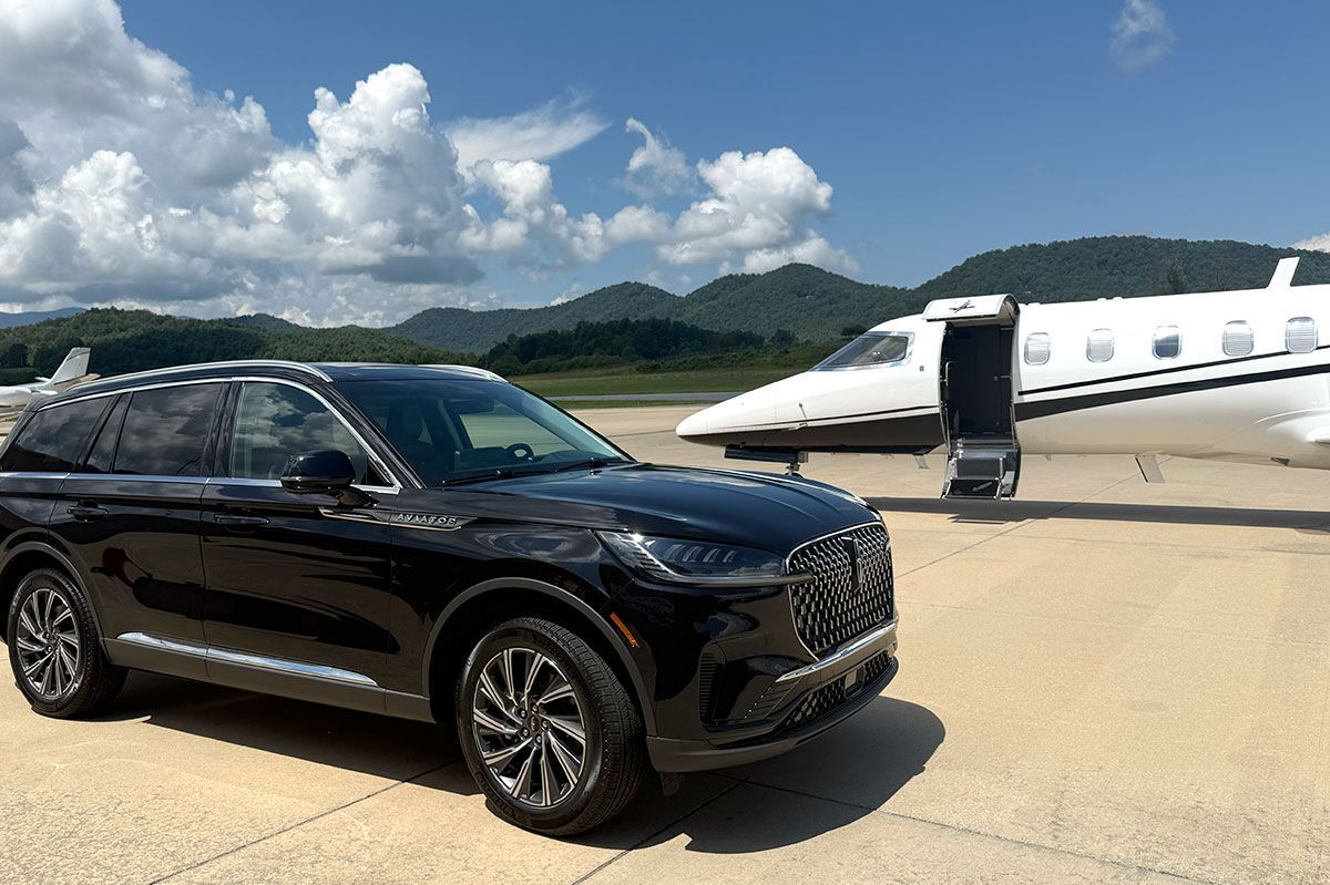 Black Lincoln Town Car parked on a paved road in a park with trees in the background.