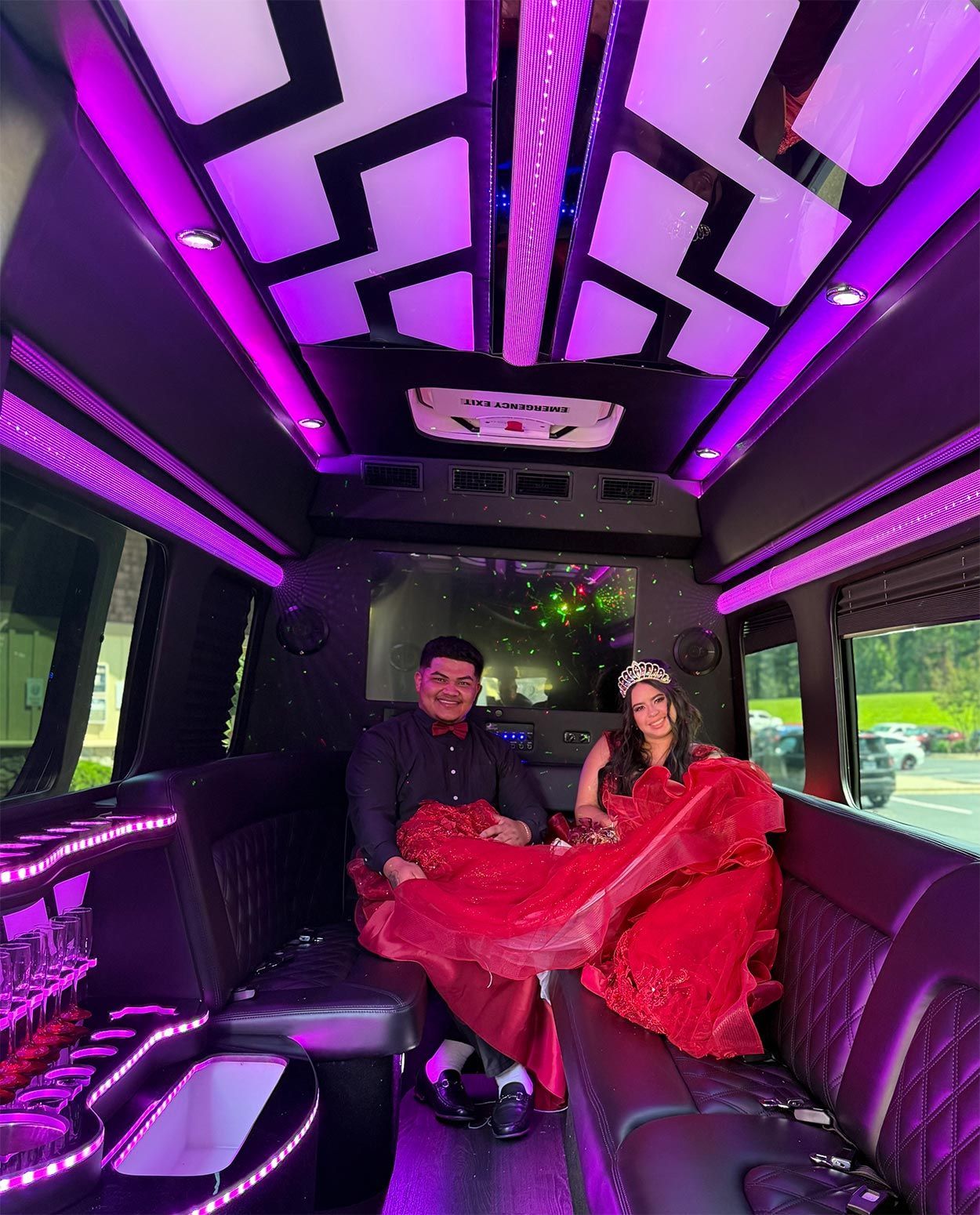 Two people seated in a sprinter limo, surrounded by purple lights, with a woman in a bright red dress