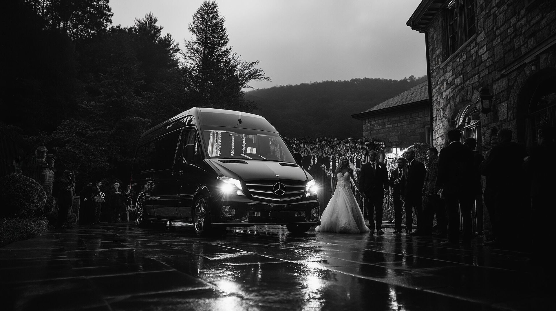 Black and white photo of a couple in the rain. A Mercedes Sprinter is parked on wet pavement. The couple is exiting their wedding.